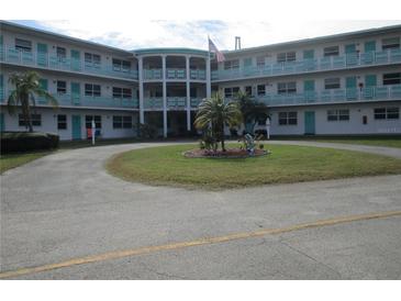 Low-angle exterior of a condominium building with a circle driveway, lawn, and U.S. flag at 1950 59Th N Ave # 212, St Petersburg, FL 33714