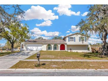 Charming two-story home featuring a well-maintained lawn, red front door, attached garage and mature trees at 1208 Briarpark Way, Valrico, FL 33596