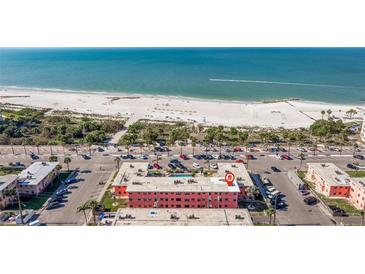 Aerial view of a pink apartment complex near a sandy beach with blue ocean water and a highway at 6800 Sunset Way # 1003, St Pete Beach, FL 33706