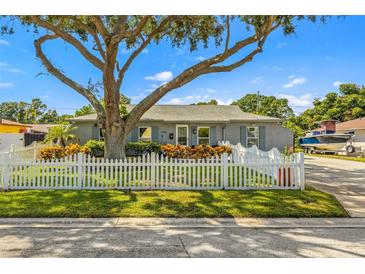 Charming gray home featuring a large tree, white picket fence, and meticulously maintained landscaping at 4135 Beach Se Dr, St Petersburg, FL 33705