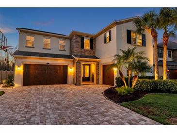 Elegant two-story home featuring a three-car garage, brick accents, and meticulously landscaped front yard at 4457 Ortona Ln, Wesley Chapel, FL 33543