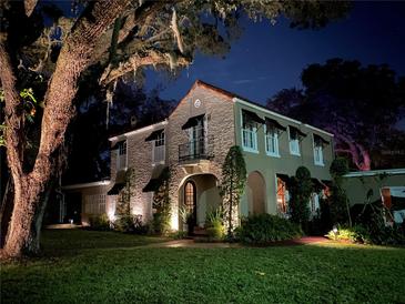 Charming two-story home with classic Spanish tile roof, black awnings, and professionally landscaped yard at night at 215 Willowick Ave, Temple Terrace, FL 33617