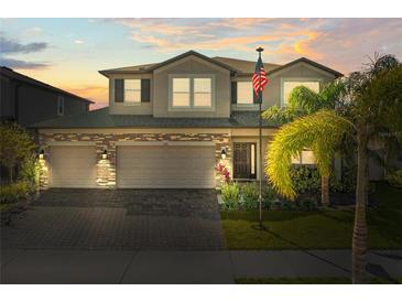 Two-story home featuring a three-car garage, brick accents, and a well-manicured lawn at sunset at 3148 Marine Grass Dr, Wimauma, FL 33598