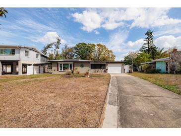 View of house with an attached one car garage on a large grassy lot and mature landscaping at 8001 Orient Ne Way, St Petersburg, FL 33702