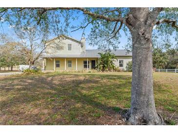Charming two-story home with a welcoming front porch and a lush green lawn surrounded by mature trees at 403 Indian Meadow Ct, Wimauma, FL 33598