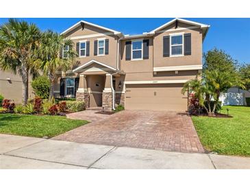 Charming two-story home showcasing a manicured lawn, stone accents, and a brick driveway at 12225 Lake Blvd, New Port Richey, FL 34655