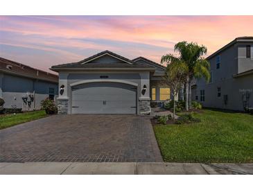 Beautiful home with lush lawn, stone accents, brick driveway and a two-car garage at sunset at 31046 Lindentree Dr, Wesley Chapel, FL 33543