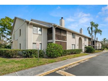 A charming condo building with tan stucco, brown balconies, well-maintained landscaping, and a glimpse of a palm tree at 2087 Hunters Glen Dr # 126, Dunedin, FL 34698