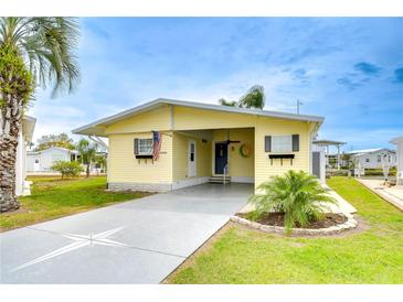 Charming yellow home featuring a covered carport, well-manicured lawn, and tropical landscaping at 35246 Tiffani Ct, Zephyrhills, FL 33541