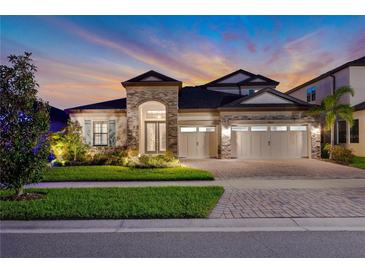 Beautiful home exterior with stone accents, manicured lawn, and three-car garage at dusk at 14522 Woodland Spur Dr, Lithia, FL 33547