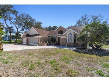 Charming single-story home featuring a three-car garage, brick accents, lush trees and meticulous landscaping at 18739 Bascomb Ln, Hudson, FL 34667