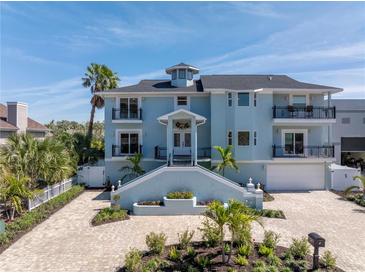 Stunning three-story blue home featuring a grand staircase, multiple balconies, lush landscaping, and brick driveway at 289 8Th N Ave, Tierra Verde, FL 33715