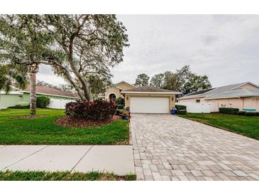 Charming home featuring a brick paver driveway leading to an attached garage and lush landscaping at 1526 River Ct, Tarpon Springs, FL 34689