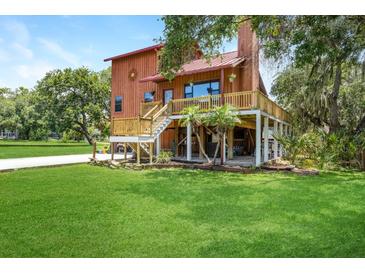 Back exterior view of a two-story home with a wooden deck and a lush lawn at 9501 Alice Ln, Riverview, FL 33578