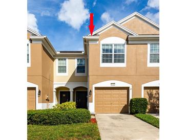 Two-story townhome featuring a tan exterior, arched front entry, a one-car garage, and neatly trimmed landscaping at 10214 Post Harvest Dr, Riverview, FL 33578