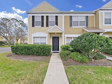 Two-story townhome featuring manicured landscaping, black shutters, tan stucco, and a welcoming walkway to the front door at 1256 Redondo Way, Wesley Chapel, FL 33543