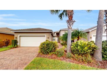 Charming single-story home with lush tropical landscaping, a paved driveway, and a two-car garage at 15644 Aurora Lake Cir, Wimauma, FL 33598