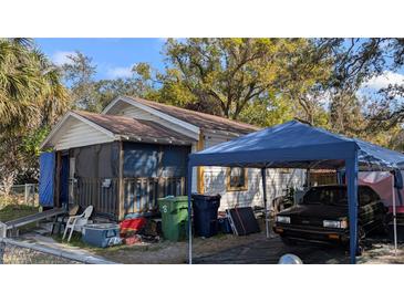 Exterior view of a home with an enclosed porch and a vehicle parked under a blue carport at 3203 N 31St St, Tampa, FL 33605
