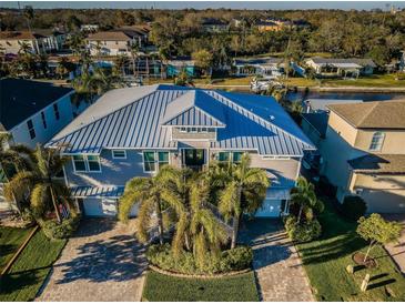 Stunning two-story home featuring a metal roof, lush landscaping, and a brick driveway that leads to a two-car garage at 315 Manatee Ln, Tarpon Springs, FL 34689