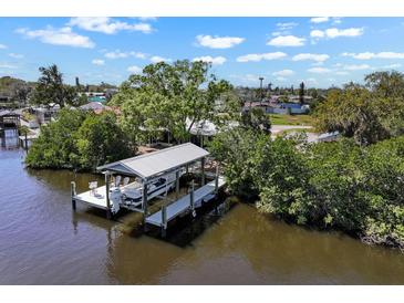 Waterfront property featuring a boat dock and lift on a sunny day, surrounded by lush greenery at 107 6Th Nw St, Ruskin, FL 33570