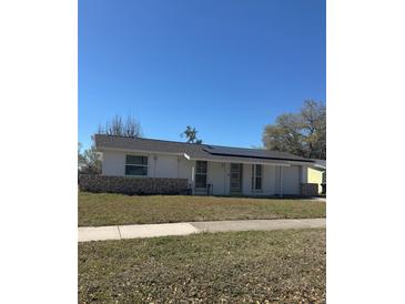 Charming single-story home featuring a stone accent wall, solar panels, and a well-maintained lawn at 1000 Hollywood Ave, Clearwater, FL 33759