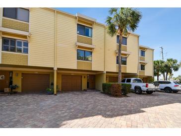 Inviting townhome showcasing a brick driveway, attached garages, and tropical palm tree landscaping at 406 Sandy Hook Rd, Treasure Island, FL 33706