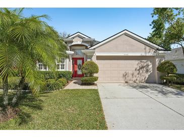 Charming home featuring a red front door, well-manicured lawn, and lush tropical landscaping at 15433 Lake Bella Vista Dr, Tampa, FL 33625