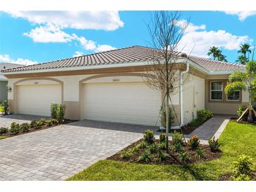Home exterior displaying a two-car garage, a paver driveway, and landscaping in front of the home under a cloudy blue sky at 20411 Symphony Pl, Venice, FL 34293