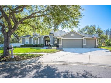 Charming single-story home featuring a three-car garage, landscaped yard, and mature shade tree at 5404 Garden Arbor Dr, Lutz, FL 33558