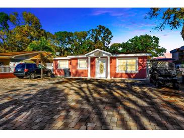 Charming single-story home with a red exterior, paver driveway, and well-maintained landscaping at 6013 N Grady Ave, Tampa, FL 33614