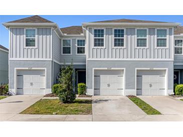 Charming two-story townhome featuring a gray exterior, a well-manicured lawn, and individual car garages at 12309 Grizzly Ln, New Port Richey, FL 34654