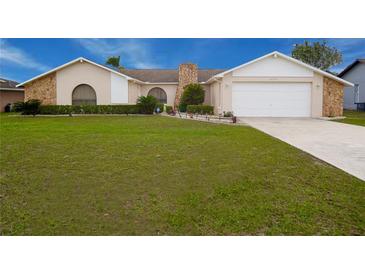 Inviting single-Gathering home featuring a well-manicured lawn, a stone chimney, and an attached two-car garage at 10440 Laval St, Spring Hill, FL 34608