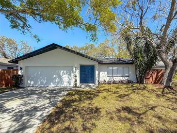 Charming home featuring a well-manicured lawn and a striking blue front door, complemented by mature trees and a two car garage at 7711 Dover N Ct, St Petersburg, FL 33709