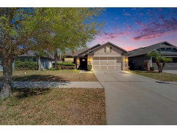 Inviting home featuring a two-car garage, stone accents, and manicured landscaping at dusk at 12220 Legacy Bright St, Riverview, FL 33578