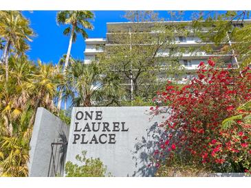 View of the condo building with lush landscaping and a vibrant red flowering bush in front at 201 W Laurel St # 212, Tampa, FL 33602