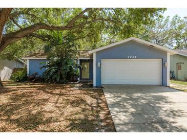 Charming home featuring a lush, landscaped yard with mature trees and a two-car garage at 1721 Sutton Pl, Dunedin, FL 34698
