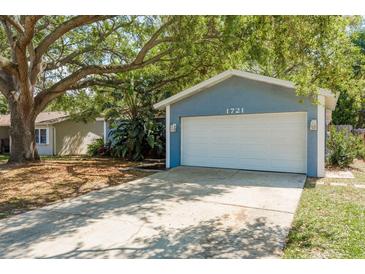 Charming home featuring an attached two-car garage and a driveway, all under the shade of mature trees at 1721 Sutton Pl, Dunedin, FL 34698