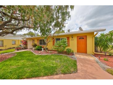 Charming yellow home with an orange door, lush green lawn, and mature landscaping at 401 Dorchester Pl # 69, Sun City Center, FL 33573