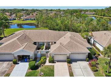 Aerial view of a well-maintained villa with a two car garage near a serene pond and lush greenery at 767 Tremont Greens Ln # 64, Sun City Center, FL 33573