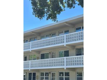 White condo building featuring three floors and decorative concrete block balcony railings under a blue sky and tree canopy at 8100 Dr Martin Luther King Jr N St # 302, St Petersburg, FL 33702