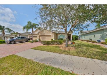 Charming tan home featuring lush landscaping, a brick driveway, and a two-car garage at 807 Chipper Dr, Sun City Center, FL 33573