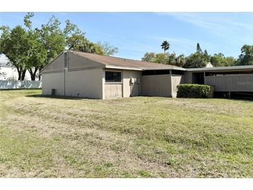 Side view of home with beige exterior, brown roof, grass lawn, and partial carport at 8711 Plum Ln, Temple Terrace, FL 33637