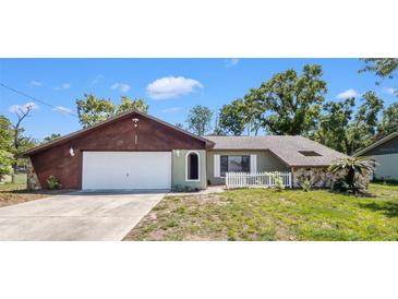 Charming single-story home featuring an attached garage, stone accents, and a cozy front yard with a white picket fence at 3276 Morven Dr, Spring Hill, FL 34609