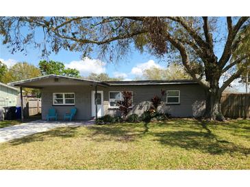 Charming single-story home featuring a manicured lawn, beautiful tree, and cozy front porch with blue chairs at 337 Shore E Dr, Oldsmar, FL 34677