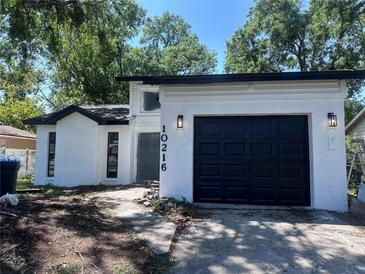 Charming home featuring a black garage door, white stucco, and modern exterior lighting fixtures at 10216 N Pawnee Ave, Tampa, FL 33617