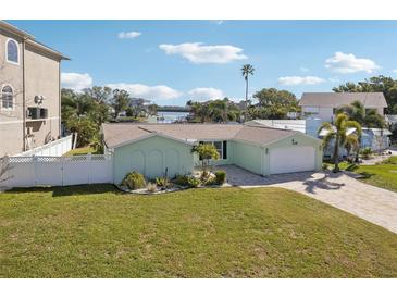 Inviting single-story home with a well-manicured lawn, palm trees, and attached two car garage at 104 Carlyle Cir, Palm Harbor, FL 34683