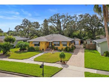 Charming yellow home featuring a well-manicured front yard, striped awnings, and brick-paved driveway at 225 Garden S Cir, Dunedin, FL 34698