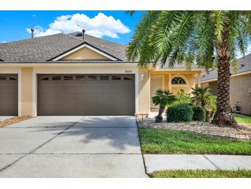 Charming one-story home featuring a two-car garage, a well-manicured lawn, and tropical landscaping with mature palm trees at 31833 Turkeyhill Dr, Wesley Chapel, FL 33543