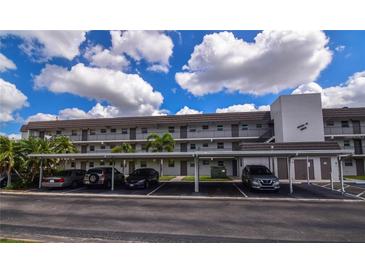 Three-story condo building features covered parking and well-maintained landscaping under a sunny sky with fluffy white clouds at 9815 47Th N Ave # 306, St Petersburg, FL 33708