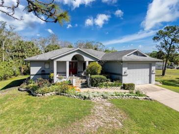 Charming single-story home with a lush front lawn, flower beds, and a two-car garage at 8437 Indies Dr, Hudson, FL 34667